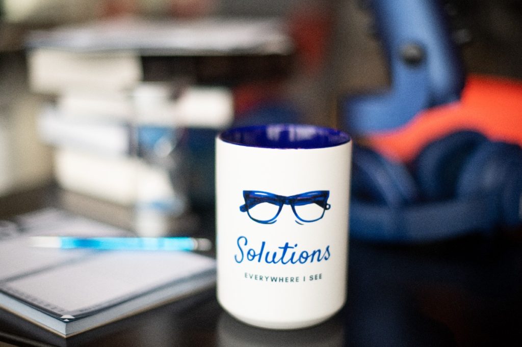 Nel Tax and Financial Solutions' mug that says Solutions everywhere I see. Blue eyeglasses frames. Blue microphone. Notepad. Textbooks tax law case books.